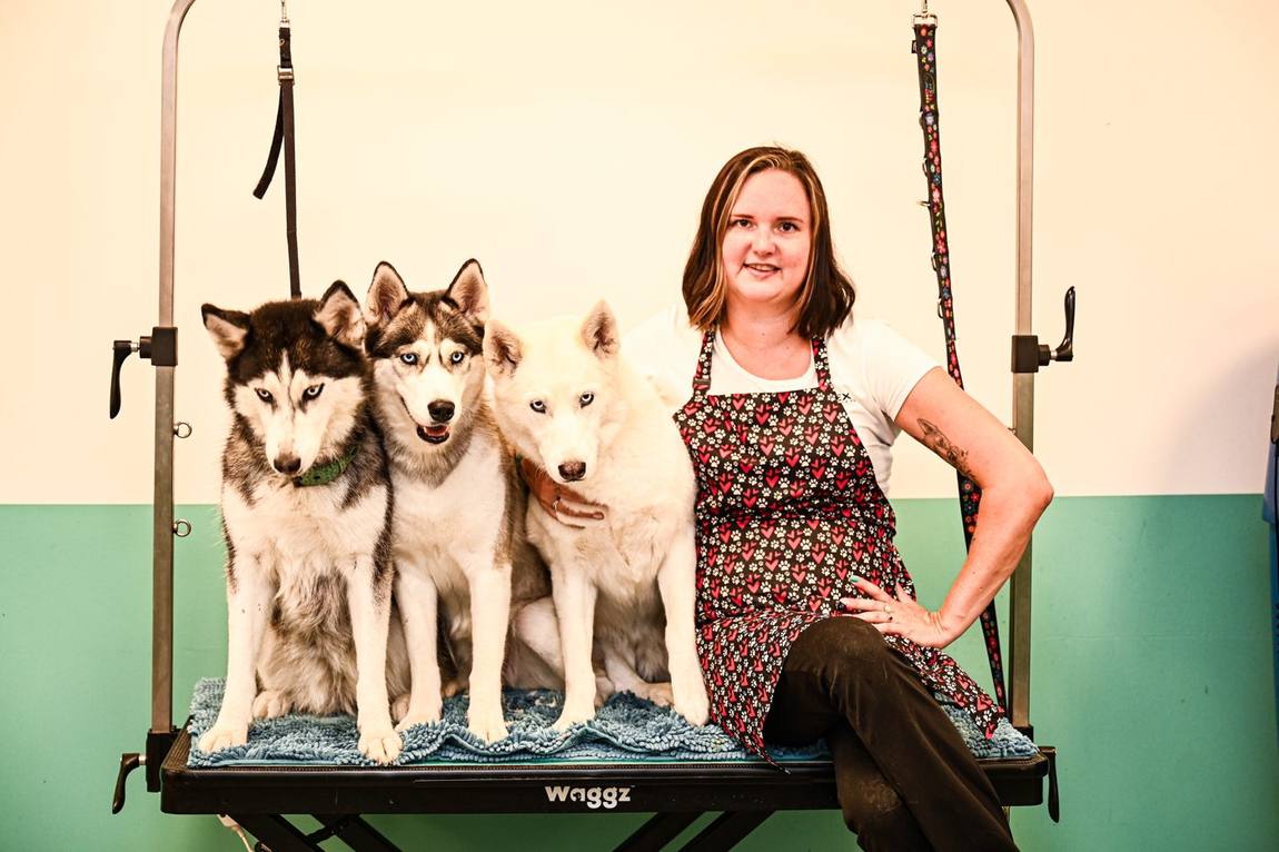 Kim zit op de trimtafel naast haar drie husky's